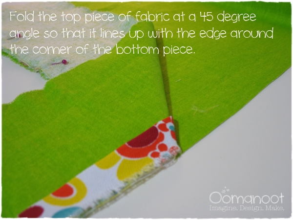 Fold the top piece of fabric at a 45 degree angle so that it lines up with the edge around the corner of the bottom piece.