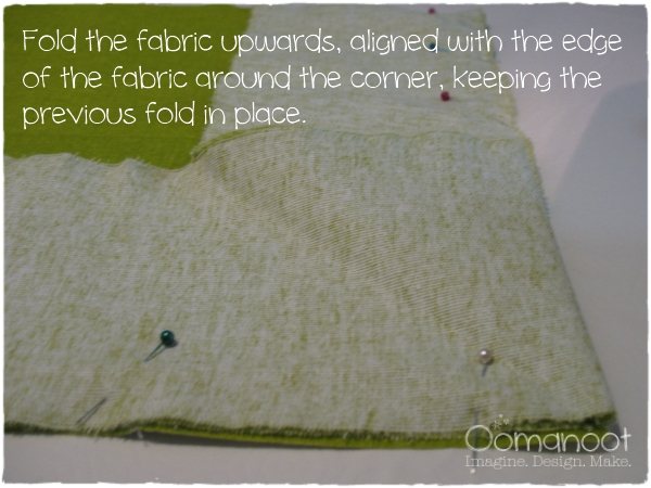 Fold the fabric upwards, aligned with the edge of the fabric around the corner, keeping the previous fold in place.